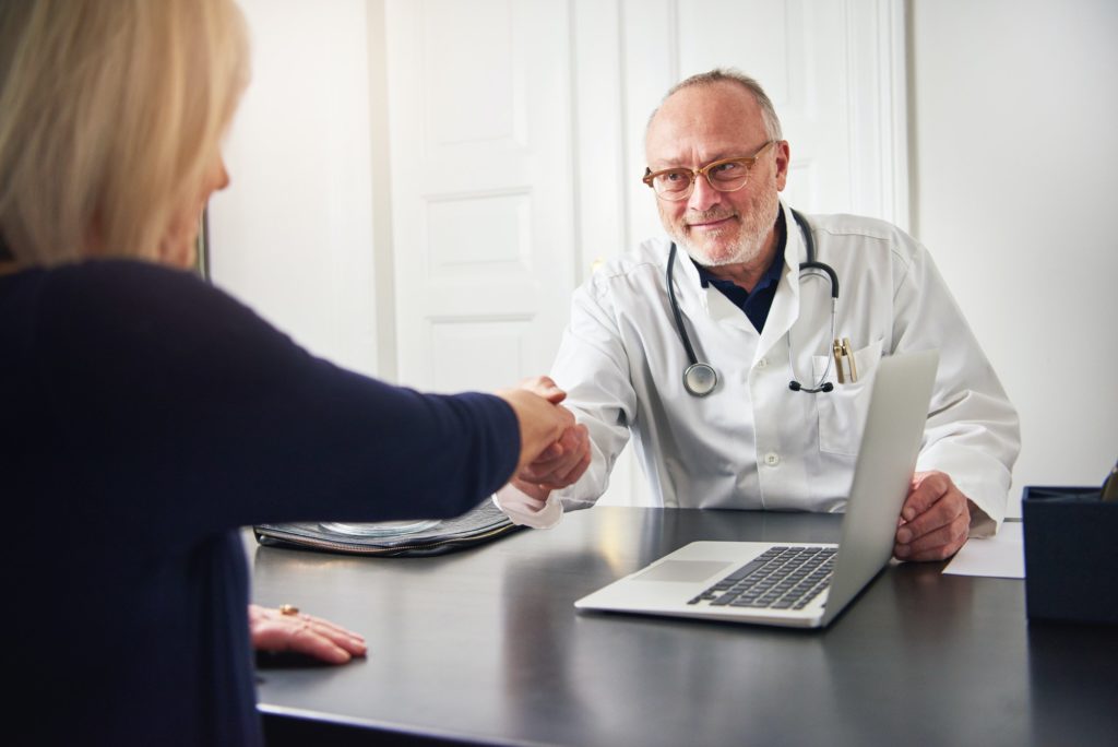 Adult medic shaking hands with patient over table