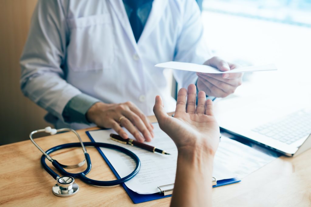 Male doctor handing a prescription to the patient.