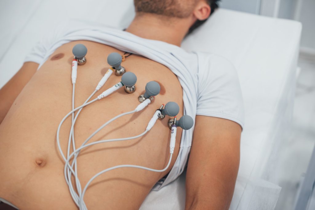 Man lying on the bed in the clinic and getting electrocardiogram test