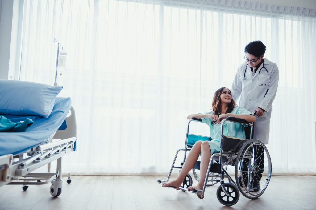 Woman patient on wheelchair in patient's room with physician's care.